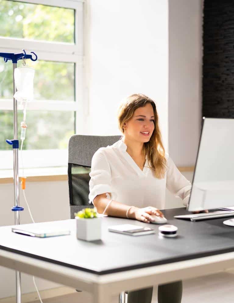 Woman Seated At Desk Receiving IV Therapy